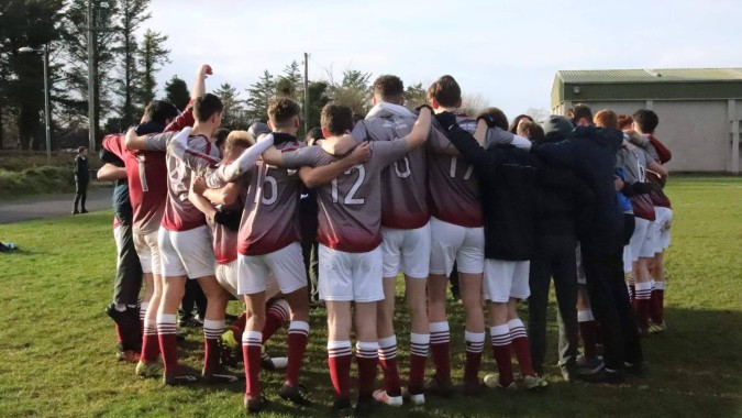 Eine Gruppe von Schülern der Grange Post Primary School steht gemeinsam in einem Kreis auf einem Rasenfeld während einer Sportaktivität.