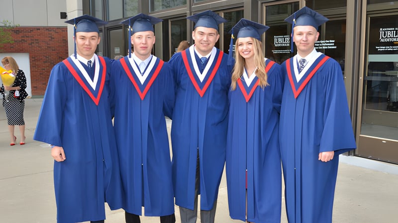 Fünf Schüler der Grant Park High School tragen blaue Abschlusskleidung vor einem Schulgebäude.