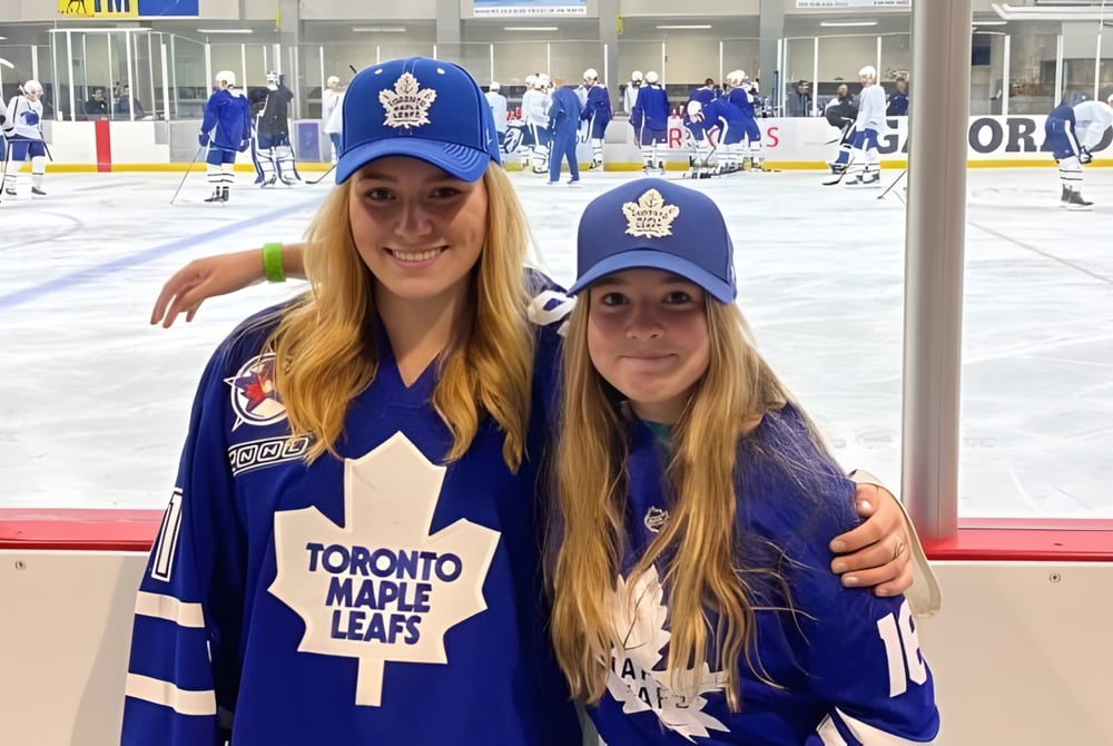 Zwei Schülerinnen der Gravenhurst High School tragen Toronto Maple Leafs Trikots und posieren vor einer Eishockeyarena.