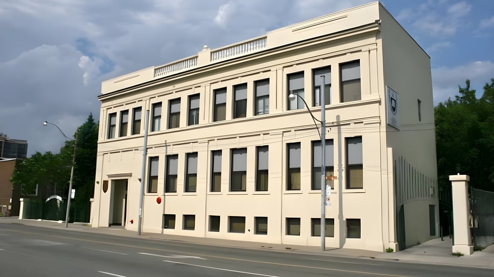 Das mehrstöckige beige Gebäude des Great Lakes College of Toronto steht an einer Straße mit Bäumen und einem bewölkten Himmel im Hintergrund.