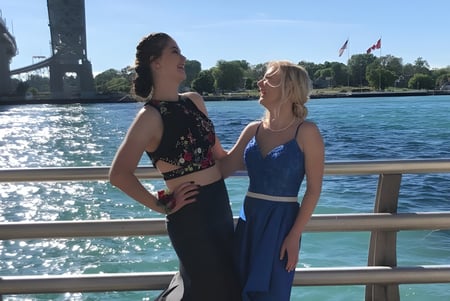 Zwei Schülerinnen der Great Lakes District Secondary School stehen auf einem hölzernen Steg mit Wasser und einer Brücke im Hintergrund.