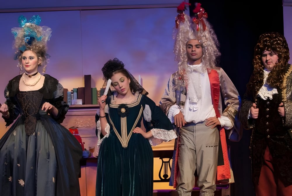 Vier kostümierte Schülerinnen und Schüler des Greater Essex County District School Board treten auf einer Bühne vor buntem Hintergrund auf.