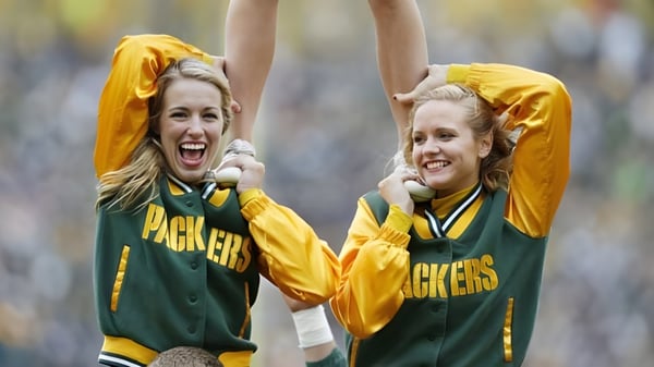 Zwei Schülerinnen des Green Bay Area Public School District jubeln im Freien in grünen und gelben Sporttrikots.