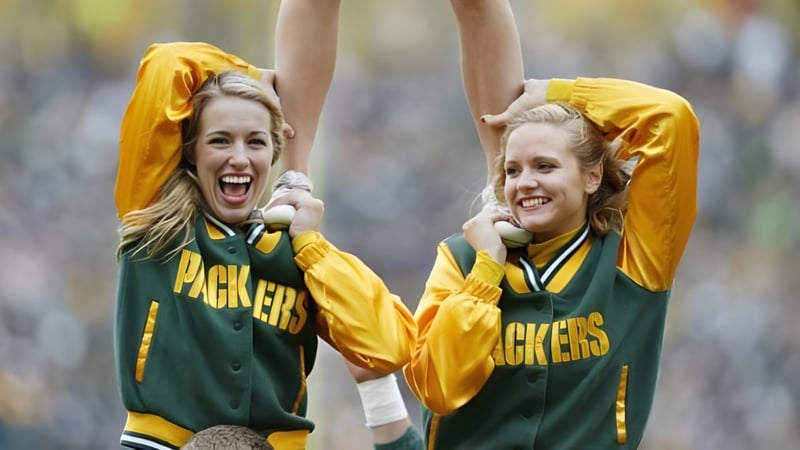 Zwei Schülerinnen des Green Bay Area Public School District jubeln im Freien in grünen und gelben Sporttrikots.