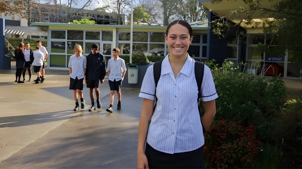 Eine lächelnde Schülerin steht im Vordergrund auf dem Campus der Green Bay High School, während eine Gruppe Schüler im Hintergrund geht.