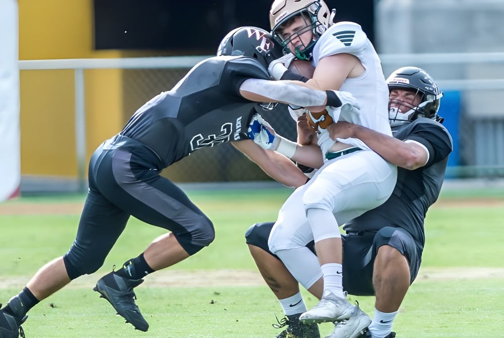 Zwei Footballspieler der Green Fields High School führen auf dem Spielfeld eine Tackling-Szene aus.