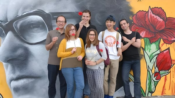 Eine Gruppe von jungen Erwachsenen steht vor einem farbenfrohen Blumenwandbild auf dem Campus von Greene's College Oxford.