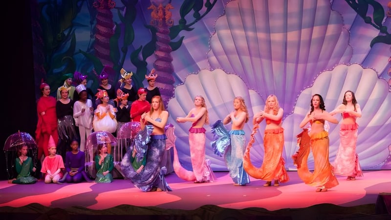 Schülerinnen der Greensboro Day School stehen in bunten Kostümen auf einer Bühne vor einem farbenfrohen Hintergund.