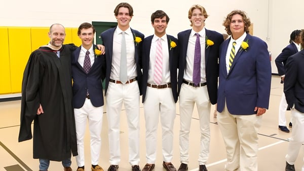 Eine Gruppe junger Schüler der Greensboro Day School steht in formeller Kleidung vor einer gelben Wand in der Schule.