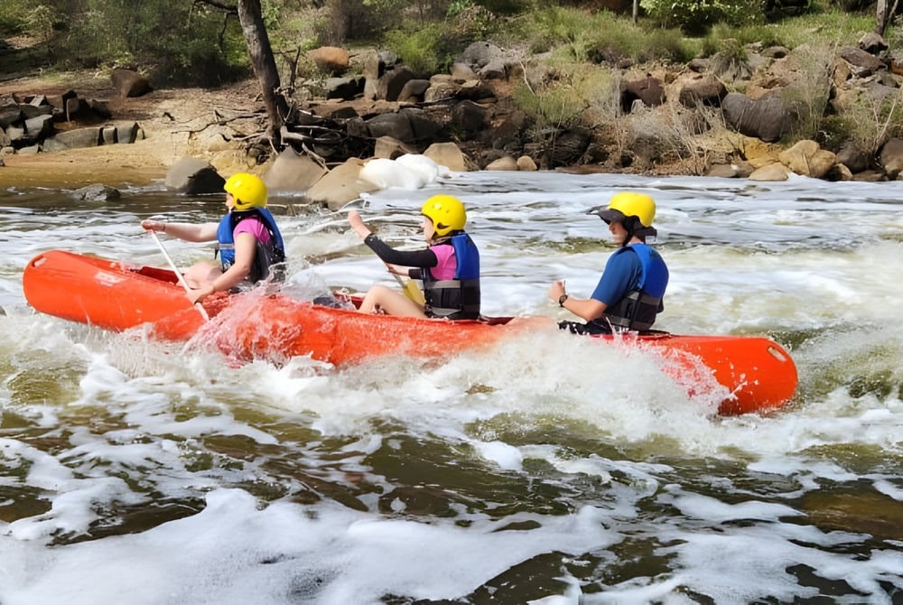 Schüler des Greenwood College navigieren mit bunten Rettungswesten und Helmen ein rotes Schlauchboot auf einem wilden Fluss.