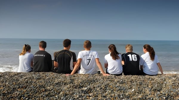 Eine Gruppe von Personen sitzt an einem Kiesstrand mit Blick auf das ruhige Meer auf dem Gelände von Gresham’s School.