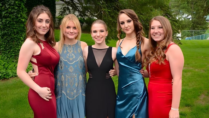 Fünf Schülerinnen der Grier School stehen in farbenfrohen Kleidern zusammen in einer grünen Außenanlage.