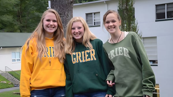 Drei Schülerinnen der Grier School stehen gemeinsam vor einem Wohngebäude und lächeln.