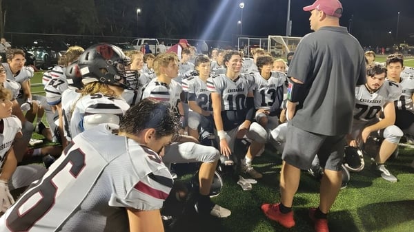 Eine Gruppe von jungen Fußballspielern des Groton-Dunstable Regional School District versammelt sich nachts auf dem Spielfeld mit einem Trainer.