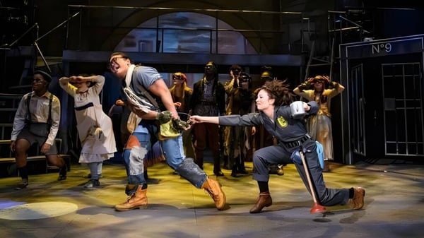 Eine Gruppe von Menschen steht auf der Bühne mit einer großen Bogenfensterkulisse auf dem Campus der Groton School.