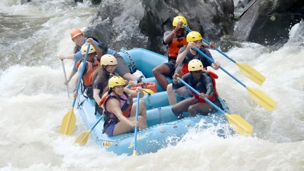 Eine Gruppe von Schülern der Groton School unternimmt eine Wildwasser-Rafting-Tour in einem blauen Schlauchboot in einer felsigen Landschaft.