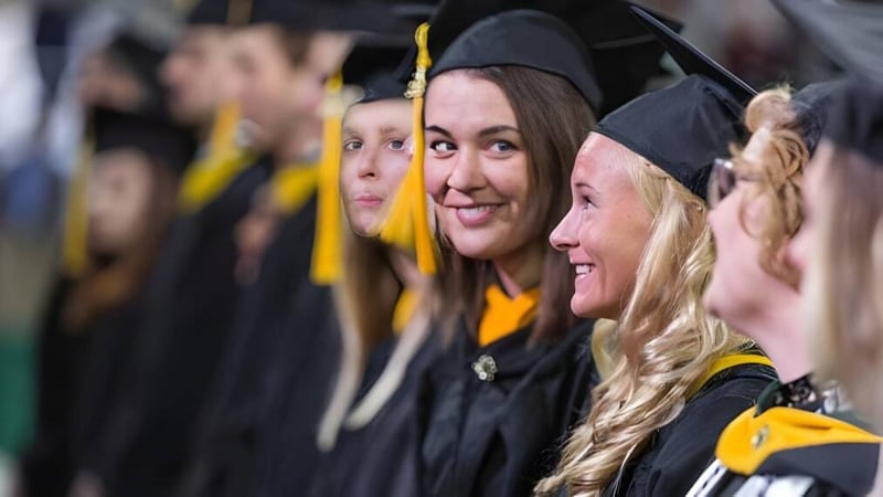 Eine Gruppe von Absolventen in schwarzen Talaren und Mörtelbrett steht zusammen bei der Abschlussfeier des Guelph Collegiate Vocational Institute.
