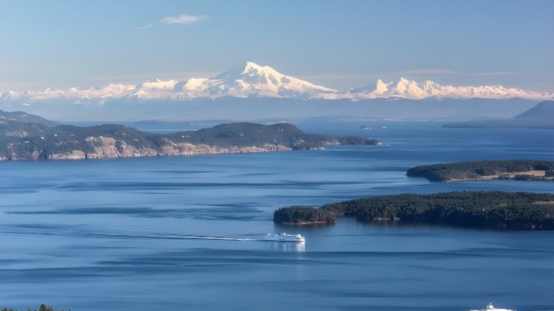 Blick auf eine ruhige Wasserfläche mit bewaldeten Inseln und schneebedeckten Bergen im Hintergrund nahe der Gulf Islands Secondary School.