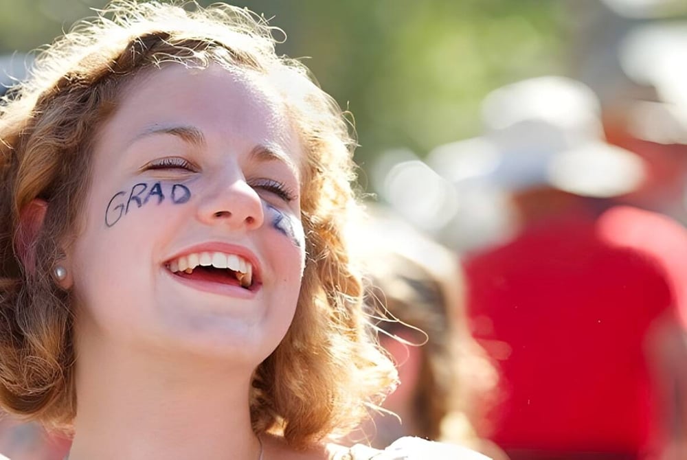 Eine junge Frau mit lockigem Haar und GRAD-Schriftzug im Gesicht feiert ihre Abschlussfeier an der Gulf Islands Secondary School.