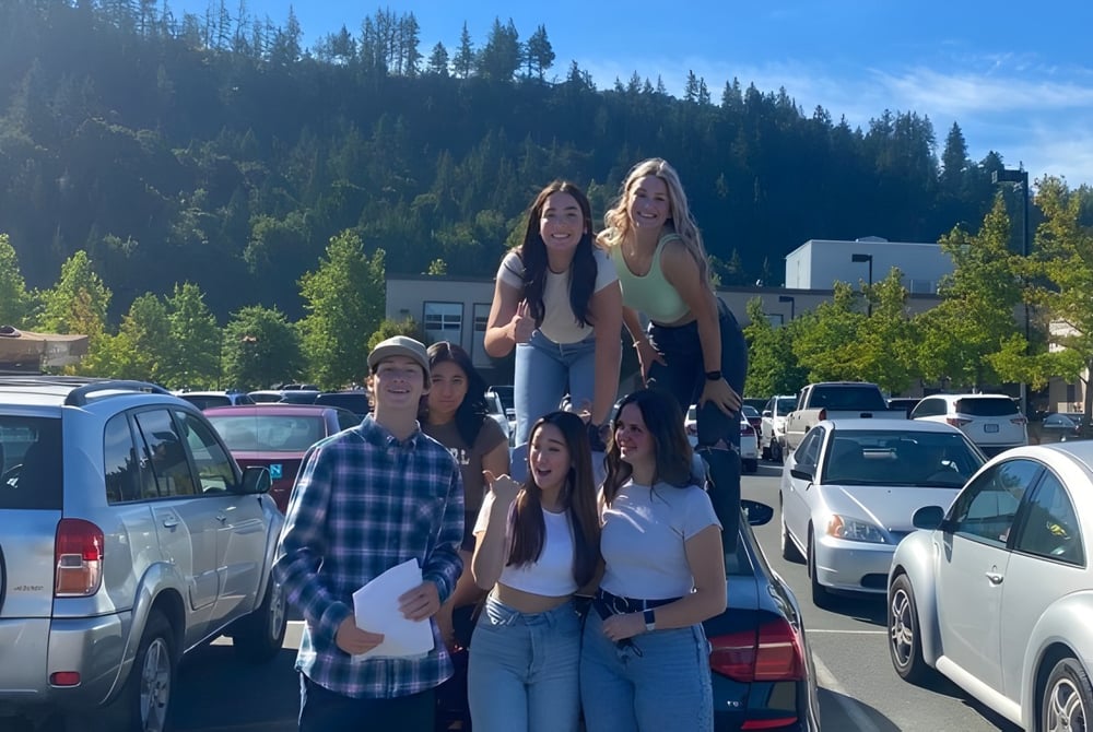 Eine Gruppe von Schülern steht auf dem Schulgelände der G.W. Graham Secondary School vor Bergen und Bäumen.