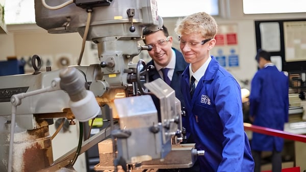 Zwei Schüler der Haberdashers' Monmouth Schools arbeiten gemeinsam an einer großen Industriemaschine in der Werkstatt.