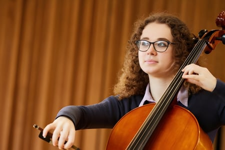 Eine Schülerin der Haberdashers' Monmouth Schools spielt Cello auf einer Bühne mit Vorhang im Hintergrund.