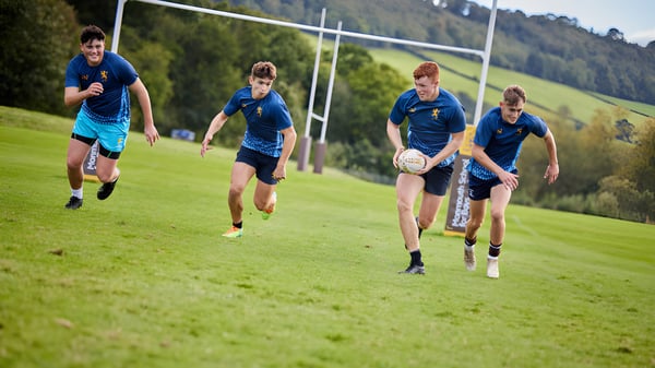 Schüler der Haberdashers' Monmouth Schools laufen auf einem Spielfeld inmitten grüner Hügel und Bäume.