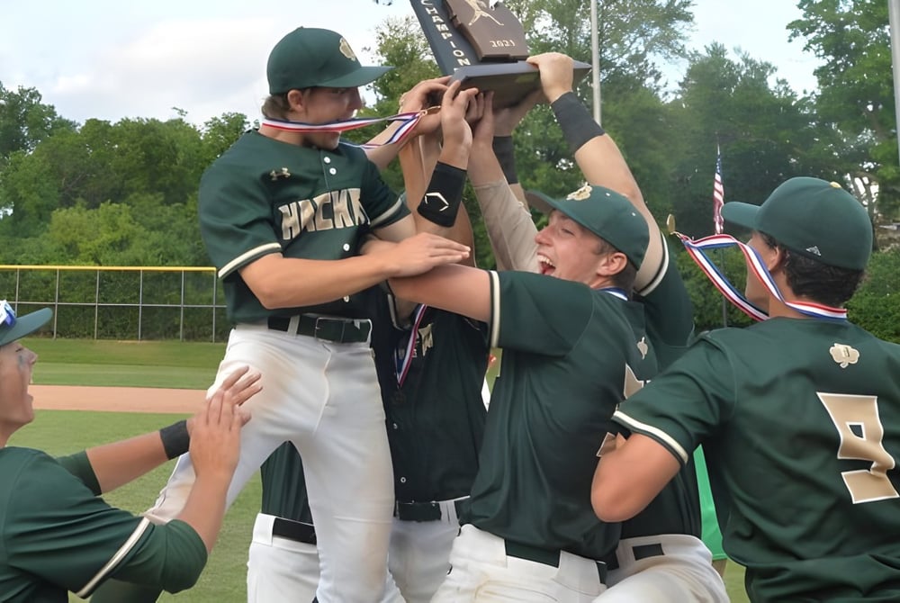 Eine Gruppe Schüler der Hackett High School in grünen Uniformen feiert gemeinsam auf dem Baseballfeld.