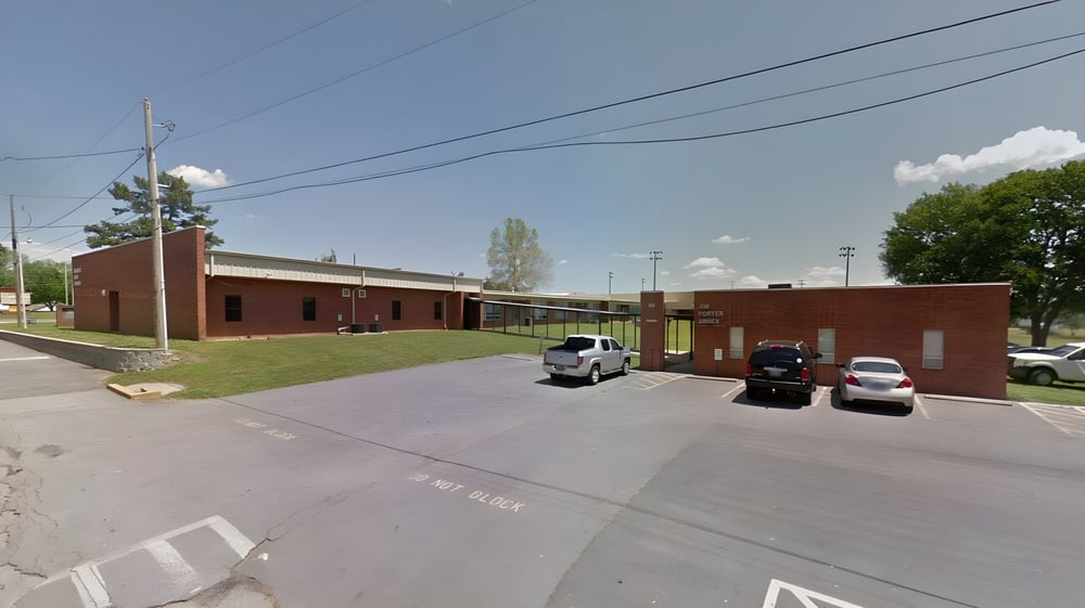 Das Backsteingebäude der Hackett High School mit Parkplatz im Vordergrund und Bäumen unter klarem Himmel.