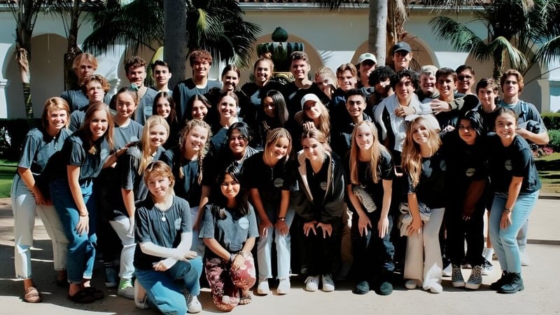 Eine Gruppe Schülerinnen und Schüler der Hackett High School versammelt sich draußen vor einem Gebäude mit Palmen im Hintergrund.