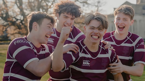 Eine Gruppe von vier Schülern der Haileybury School steht in Rugby-Uniformen in einem bewaldeten Außenbereich.