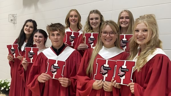 Eine Gruppe von Absolventinnen und Absolventen in roten Talaren hält ihre Diplome vor einer weißen Wand auf dem Campus der Haliburton Highlands School.