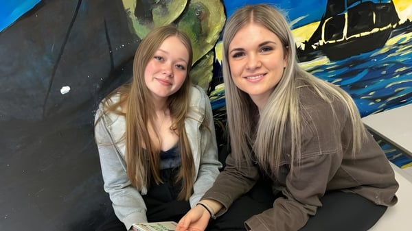 Zwei Schülerinnen der Haliburton Highlands School posieren vor einem bunten abstrakten Wandbild.