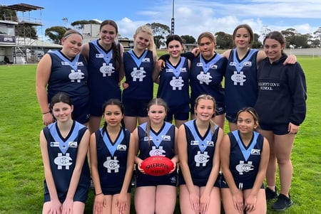 Eine Gruppe junger Sportlerinnen posiert auf dem Rasenfeld vor dem Sportstadion der Hallett Cove School.
