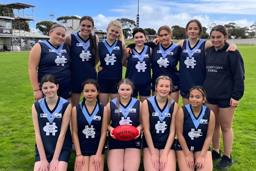 Eine Gruppe junger Sportlerinnen posiert auf dem Rasenfeld vor dem Sportstadion der Hallett Cove School.