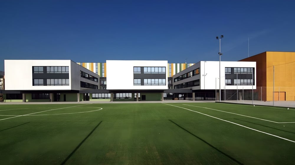 Das moderne Gebäude der Hamelin-Laie International School mit dem großen Sportfeld im Vordergrund unter klarem blauem Himmel.