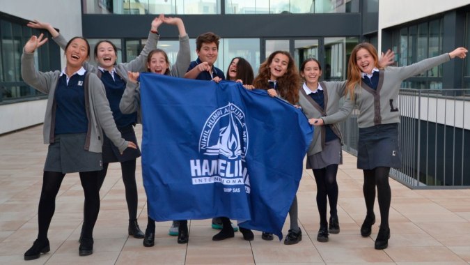 Schüler der Hamelin-Laie International School halten gemeinsam eine große blaue Fahne mit dem Schriftzug Hazelip.