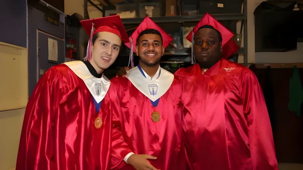Drei Absolventen in roten Talaren stehen im Flur der Hamilton Boy's High School zusammen.