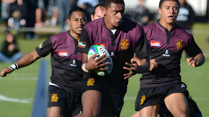 Drei Rugbyspieler der Hamilton Boy's High School laufen auf dem grasbewachsenen Spielfeld während weitere Spieler im Hintergrund zu sehen sind.