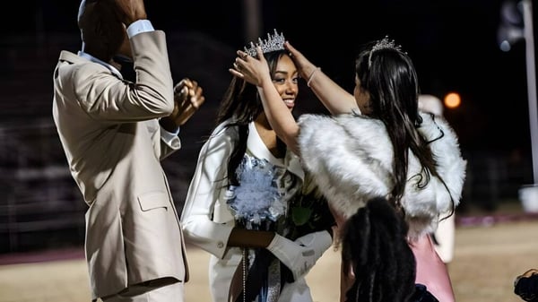 Eine Frau mit Krone und Pelzmantel bei einer Feier an der Hamilton Christian Academy mit zwei weiteren Frauen.