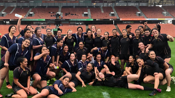 Eine große Gruppe Schülerinnen der Hamilton Girl's High School steht gemeinsam auf dem Fußballfeld vor einem Stadion.