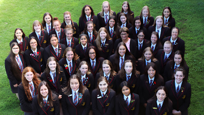 Eine Gruppe von Schülerinnen der Hamilton Girl's High School steht gemeinsam auf einem grasbewachsenen Feld.