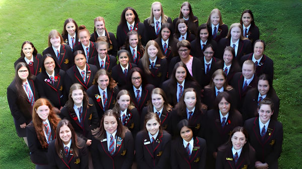 Eine große Gruppe von Schülerinnen der Hamilton Girl's High School steht auf einem grasbewachsenen Feld.
