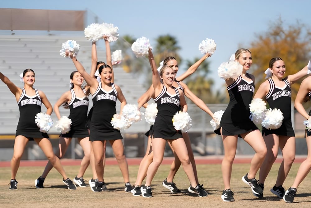 Eine Gruppe Cheerleader der Hamilton High School führt eine Aufführung auf dem Sportfeld vor dem Stadion durch.