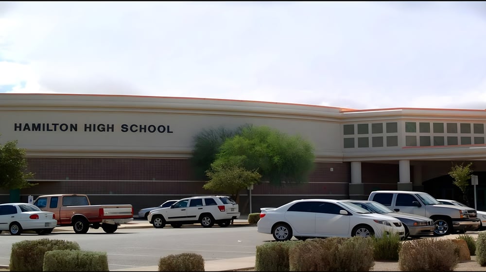 Das große Backsteingebäude der Hamilton High School mit dem Schriftzug am Gebäude und einem Parkplatz im Vordergrund.