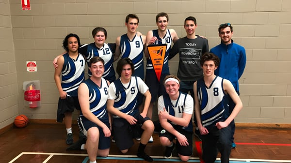 Eine Gruppe Schülerinnen und Schüler der Hamilton Secondary College posiert als Basketballmannschaft in der Sporthalle.