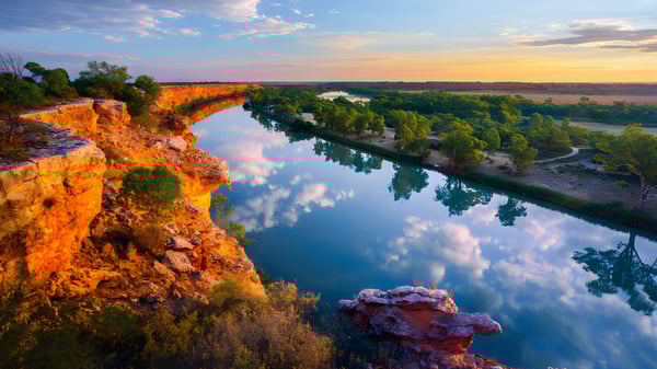 Eine ruhige Flusslandschaft in einem bewaldeten Tal bei Sonnenuntergang.