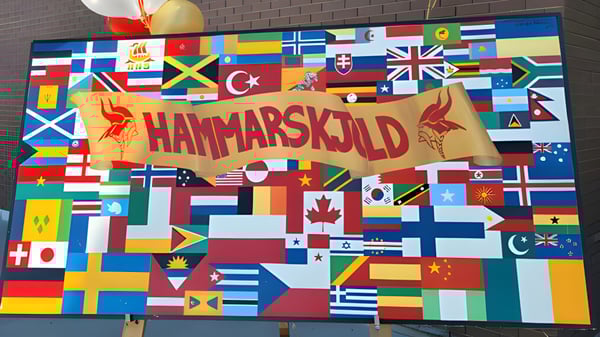 Ein großes Banner mit dem Schriftzug Hammarskjold High School umgeben von einer Collage aus verschiedenen Nationalflaggen.