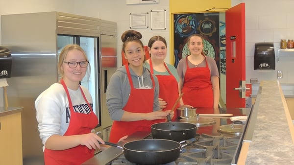 Vier Schülerinnen der Hammarskjold High School stehen in einer Küche und bereiten gemeinsam Essen zu.