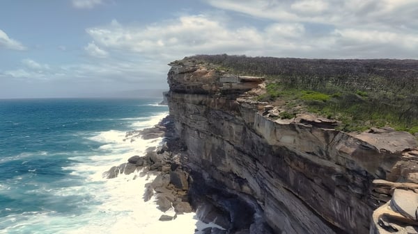 Blick auf eine felsige Klippe mit dichter Vegetation und dem türkisfarbenen Meer im Hintergrund auf dem Gelände der Hampton Senior High School.